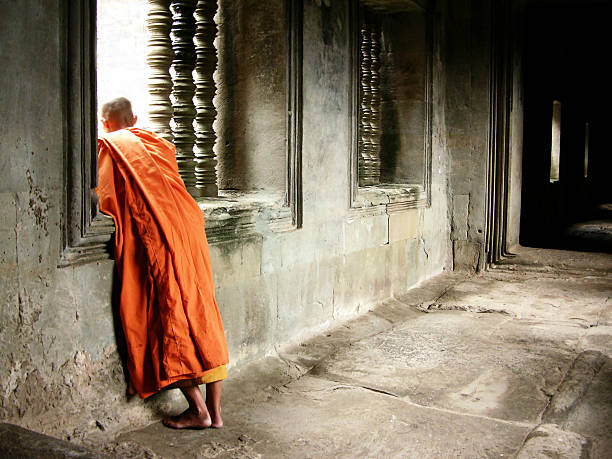 Monk in orange robe looking out window stock photo