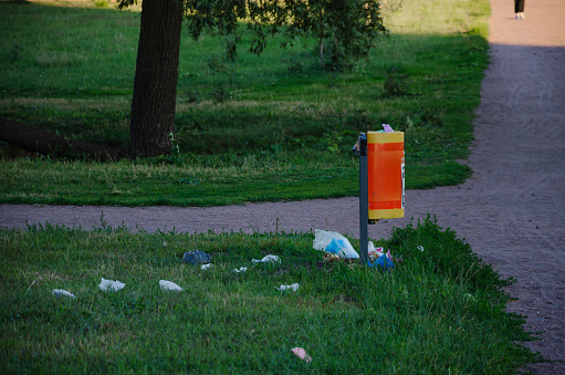 Garbage is scattered on the lawn near a garbage barrel. High quality photo