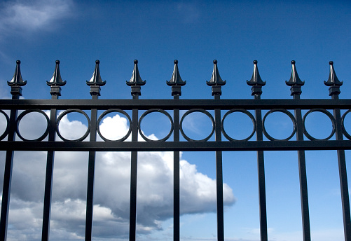 Black wrought iron fence against blue sky. We have this image in a vertical composition as well.