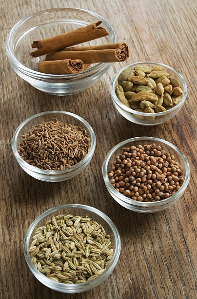 A selection of spices, cinnamon, cardomom,coriander,fennel in glass bowls, photographed in daylight on a wooden tabletop.