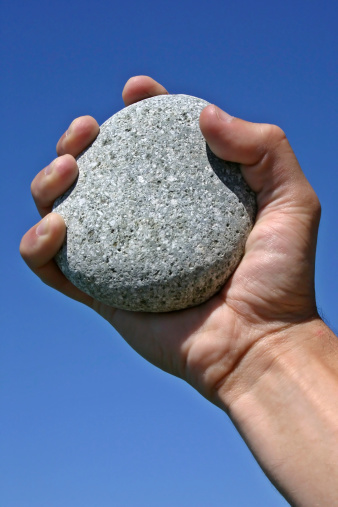 A stone clenched in a man's hand on a blue sky background