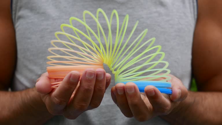 A rainbow coil spring. A person playing with a slinky. Person playing with a spiral toy. Person playing with a colorful slinky. Rainbow spring slinky. Plastic colorful spring. Plastic coil spring toy