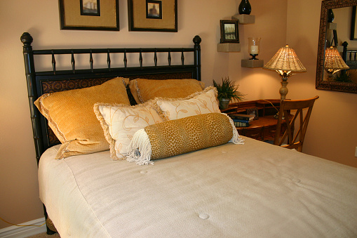 Comfortable cozy bedroom with pillows and lamp. Gold tones.