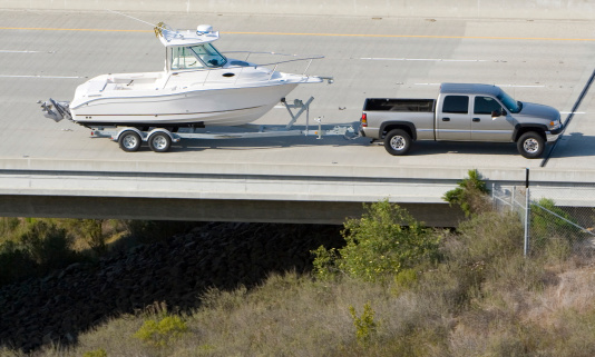 A big pick up truck pulls a new fishing boat down the highway.