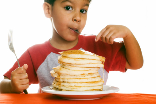 Small boy eating a huge stack of pancakes.