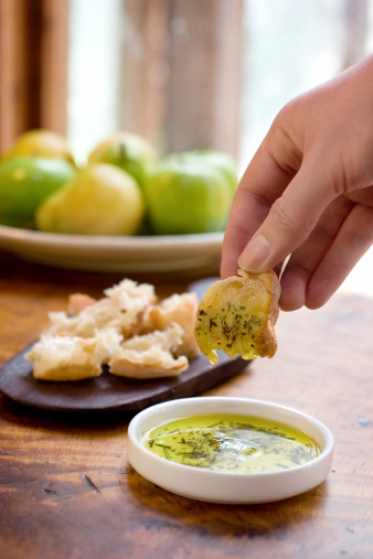 A man's hand dipping a piece of bread into herbed olive oil, there is an indentation in the oil from a falling drop.  Shallow dof.