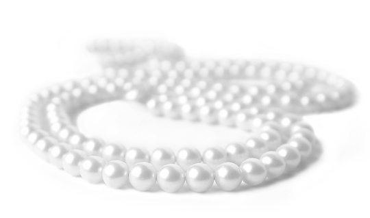 Black and white close up image of a pearl necklace on a white background. Shallow depth of field. The front and center six pearls are in sharp focus and then quickly fades.