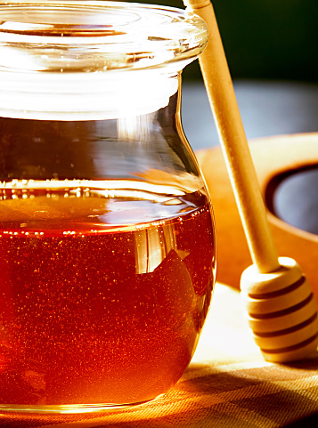 Sweet honey in the early morning light.  the honey dripper stands ready to serve your morning toast a healthy slathering of this delicious sticky sweet treat. shallow DOF.