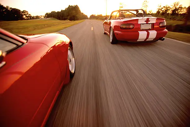 Two convertables driving side by side driving down the road with motion blur