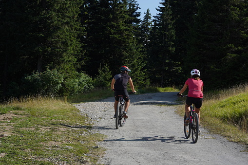 Martin, Slovakia, 08 16 2023, Man and woman are riding mountain bikes on a land road. There are many potholes on the road. The cyclists are heading to a coniferous forest where the road ends.
