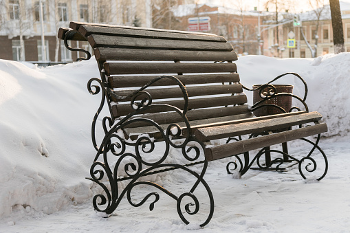 Street bench in the park covered with snow in city or town. Copy space and empty place for text and advertising.
