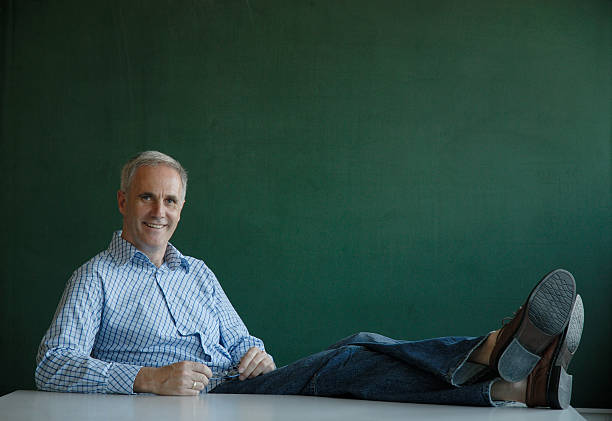 enseignant avec ses jambes sur le bureau - human leg jeans converse shoe photos et images de collection