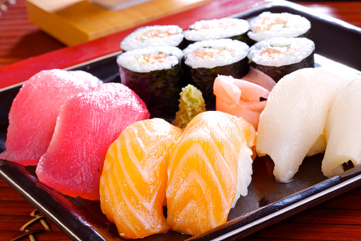 Set of sushi rolls on bamboo serving tray. Uramaki and futomaki roll close-up. Serving Japanese food. Popular Asian dish of rice and seafood on black background.