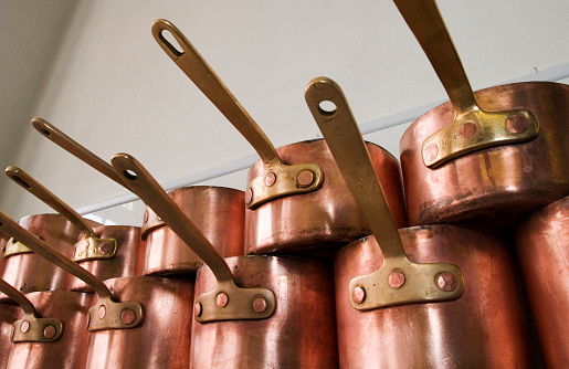 A selection of copper pans on a shelf in a proffessional kitchen.