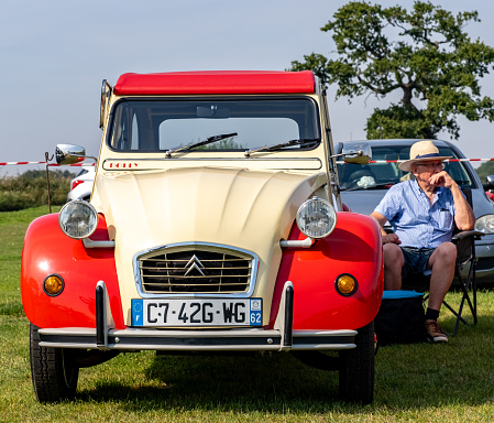 Wroxham, Norfolk, UK  September 10 2023. The owner of a vintage Citroen 2CV car sitting beside his car on display at an outdoor classic car show