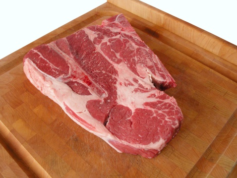 A chuck steak on wood cutting board