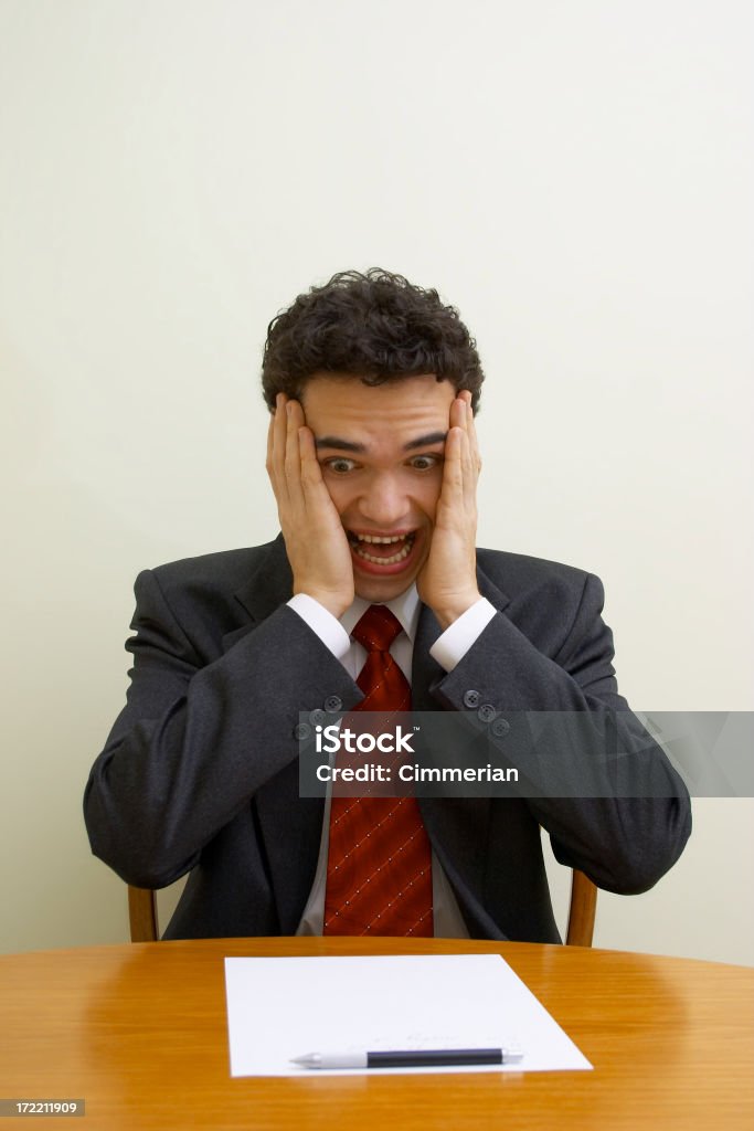 Business emotions - Shock A young businessman is sitting at a polished table looking at some document with a shocked expression. Document Stock Photo