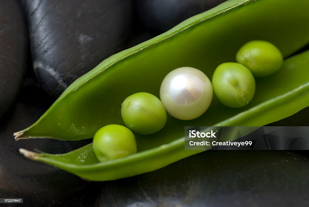 Treasure under Pearl in sweet pea pod on black river stones Individuality Stock Photo