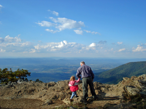 Senior with granddaughter hiking in the mountains, climbing up to a terrific view in Shenandoah National Park.