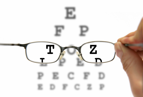 Optometrist giving a pair of eye glasses to patient and a snellen chart in the background 