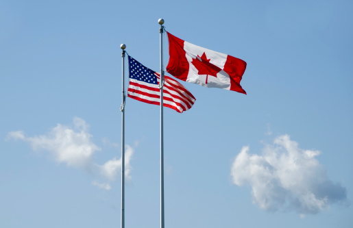 us and canadain flag blowing in the wind on blue sky