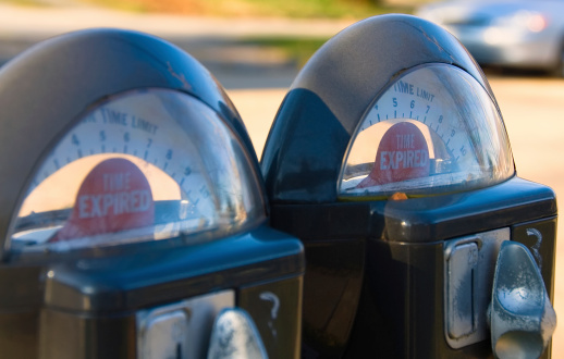 Two worn expired parking meters with car in background