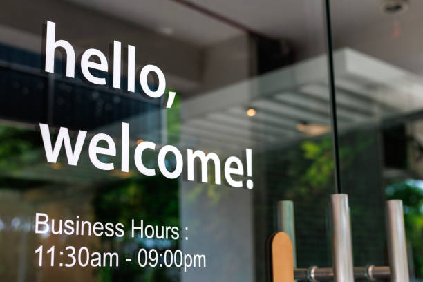 小売店のガラスドアに「こんにちは」と「ようこそ」のステッカーサインのクローズアップで、中小企業のコンセプトを象徴しています。