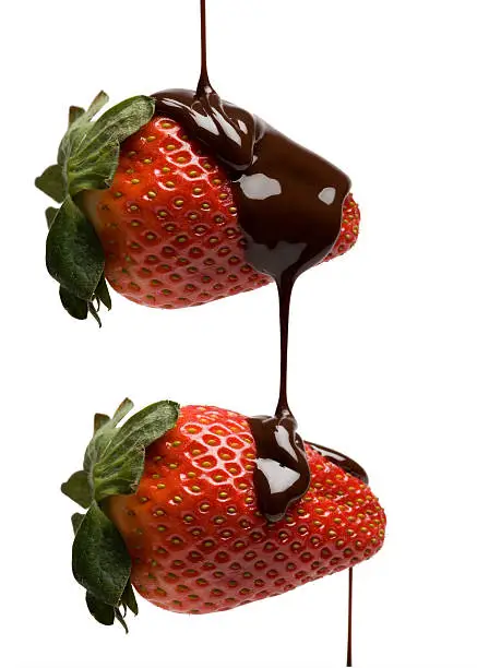 Two strawberries being dripped with chocolate isolated on white background