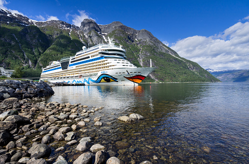 A ferry navigates the waters of Geirangerfjord between the villages of Geiranger and Hellesylt during a summer afternoon.