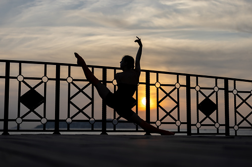 Pretty young athlete woman is stretching on the outside at sunset.