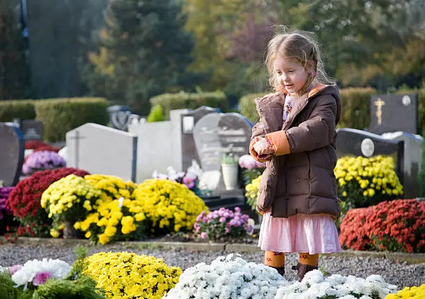 "Little 4 year old girl, standing at a gravestone, surrounded by flowers."