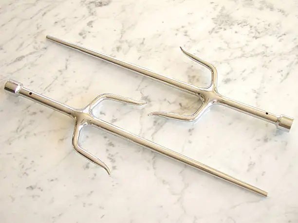 A pair of martial arts weapons known as sais on a marble background. These sais have a chrome finish.