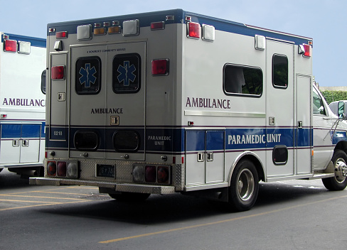 Backside of an ambulance that is flanked by a 2nd ambulance. They are parked outside a hospital emergency room.