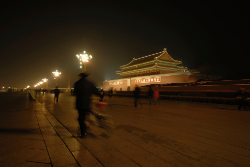 An elderly man walks past the gates to the Forbidden City,. Film grain.