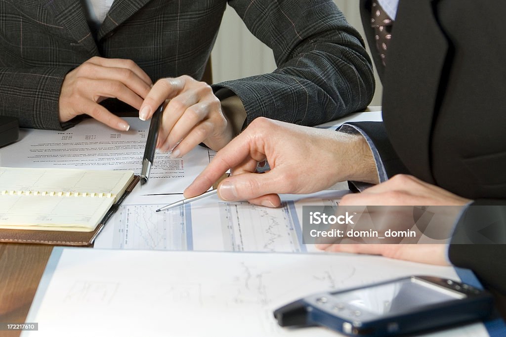 Business woman and man with pens and papers "Business Meeting, man's and woman's hands pointing on graphs." Investment Stock Photo