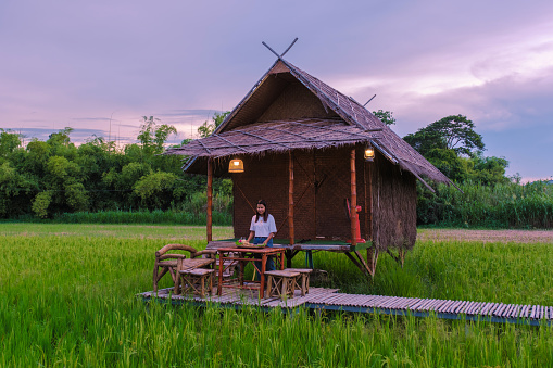 Asian Thai woman on vacation at a small homestay at the farm with a green rice paddy field in Central Thailand