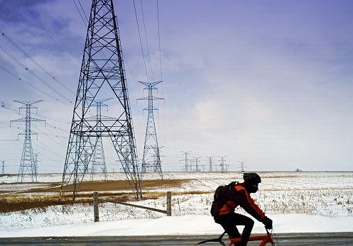 A cyclist travels past a series of hydro field towers on his bike in winter. He was intentionally blurred by the photographer to show motion.