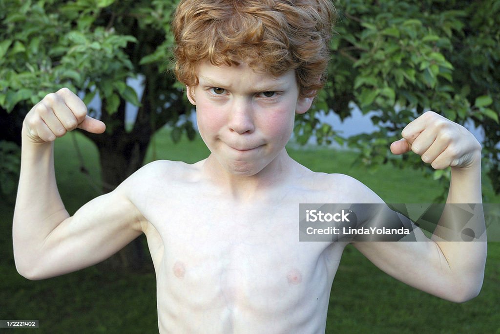 Strength Nine-year-old boy shows off his muscles.He is strong and growing like the tree in the background.Great facial expression! 8-9 Years Stock Photo