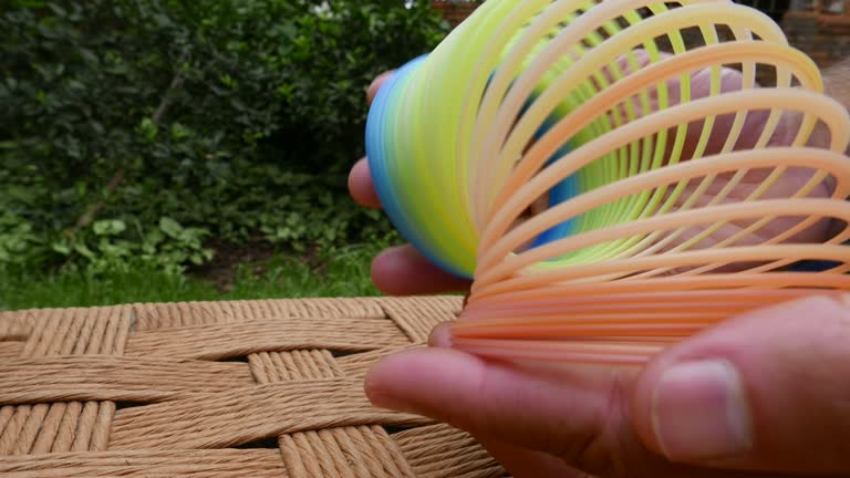 Close-up shot of a rainbow coil spring. A person playing with a slinky. Person playing with a spiral toy. Person playing with a colorful slinky. Rainbow spring slinky. Plastic colorful spring. Plastic coil spring toy