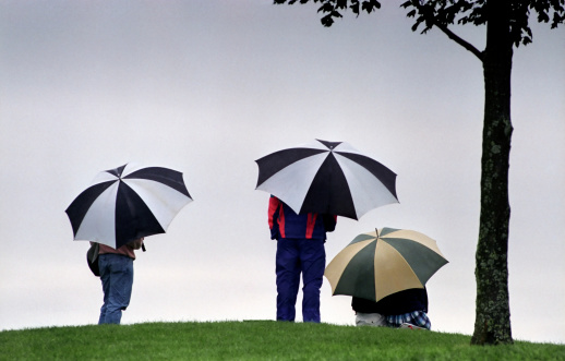 Golfers wait for their turn to tee-off under their umbrellas in the autumn rain.