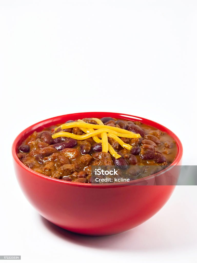 A red bowl full of chili on a white background A hot generous helping of fresh homemade spicy chili with beans, hearty beef, sweet onion, and fresh tomato topped with shredded cheddar cheese. Chili Con Carne Stock Photo