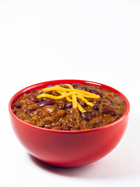 A red bowl full of chili on a white background A hot generous helping of fresh homemade spicy chili with beans, hearty beef, sweet onion, and fresh tomato topped with shredded cheddar cheese. chili con carne photos stock pictures, royalty-free photos & images