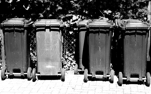 many black and white of Dark garbage cans stand closed against the fence