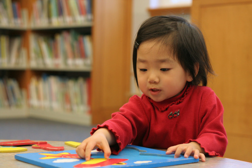 A cute little Asian girl doing a puzzle in a library.