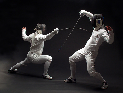 two fencers in action on black background