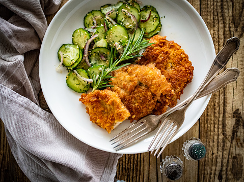 Breaded seared chicken cutlets with fresh vegetable salad on wooden table