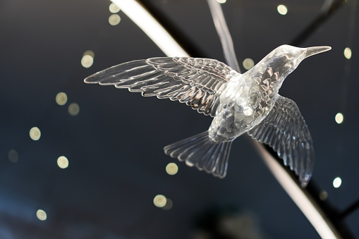 Hanging glass flying bird figurine photographed from below angle with bokeh backgrounds. Bird statue sculpture made of glass material. Empty blank copy text space.