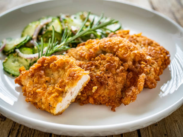 istock Breaded seared chicken cutlets with fresh vegetable salad on wooden table 1722270766