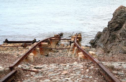 extremely rusted railway tracks are pictured heading into water.