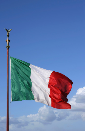 The Italian flag waving in the clear sky as a symbol of independence, spreading light and peace around.